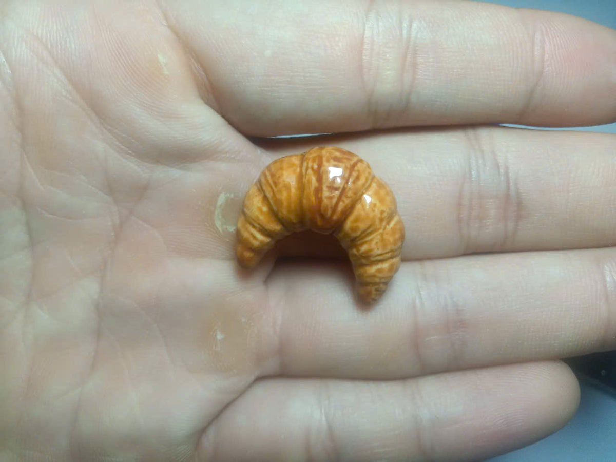 French ceramic croissant fève held between fingers